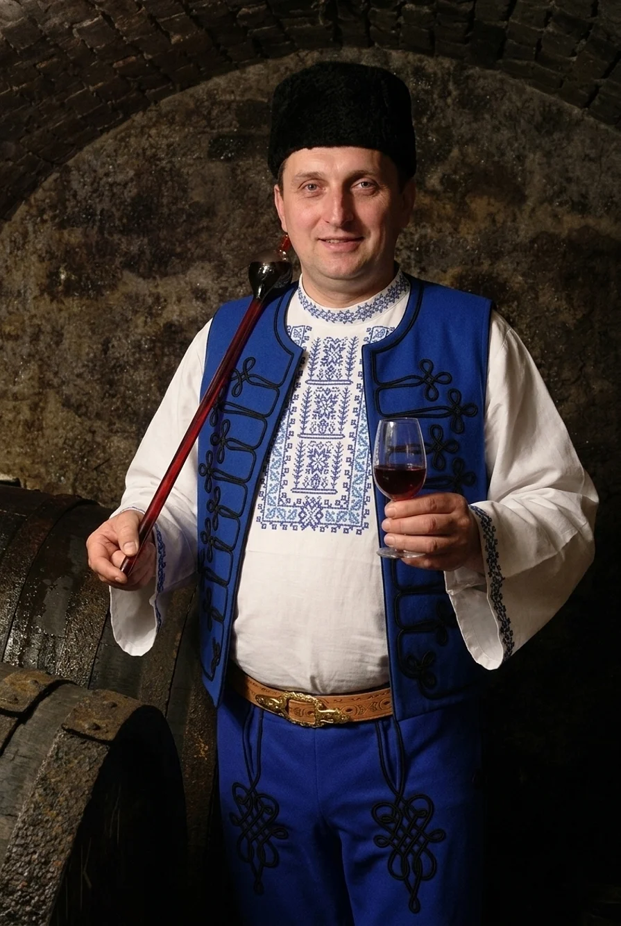 Ochutnávka vína v kamennej pivnici, muž naberá víno zo suda do hevera